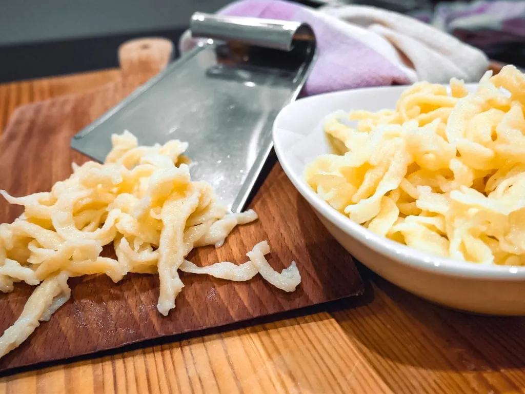 Eine Nahaufnahme von frisch zubereiteten Spätzle, die auf einem Holzbrett und in einer weißen Schüssel serviert werden.