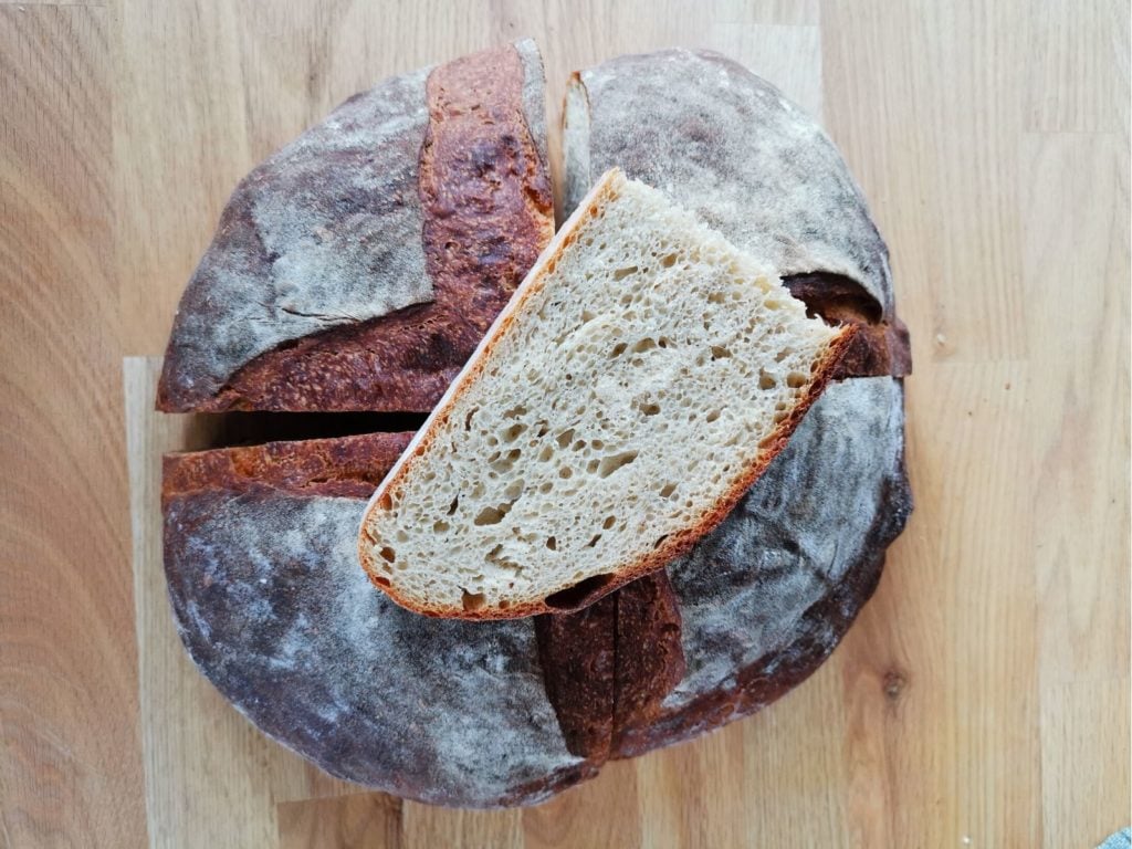 Ein rundes Kartoffelbrot mit einer knusprigen Kruste, auf einem Holzbrett serviert.