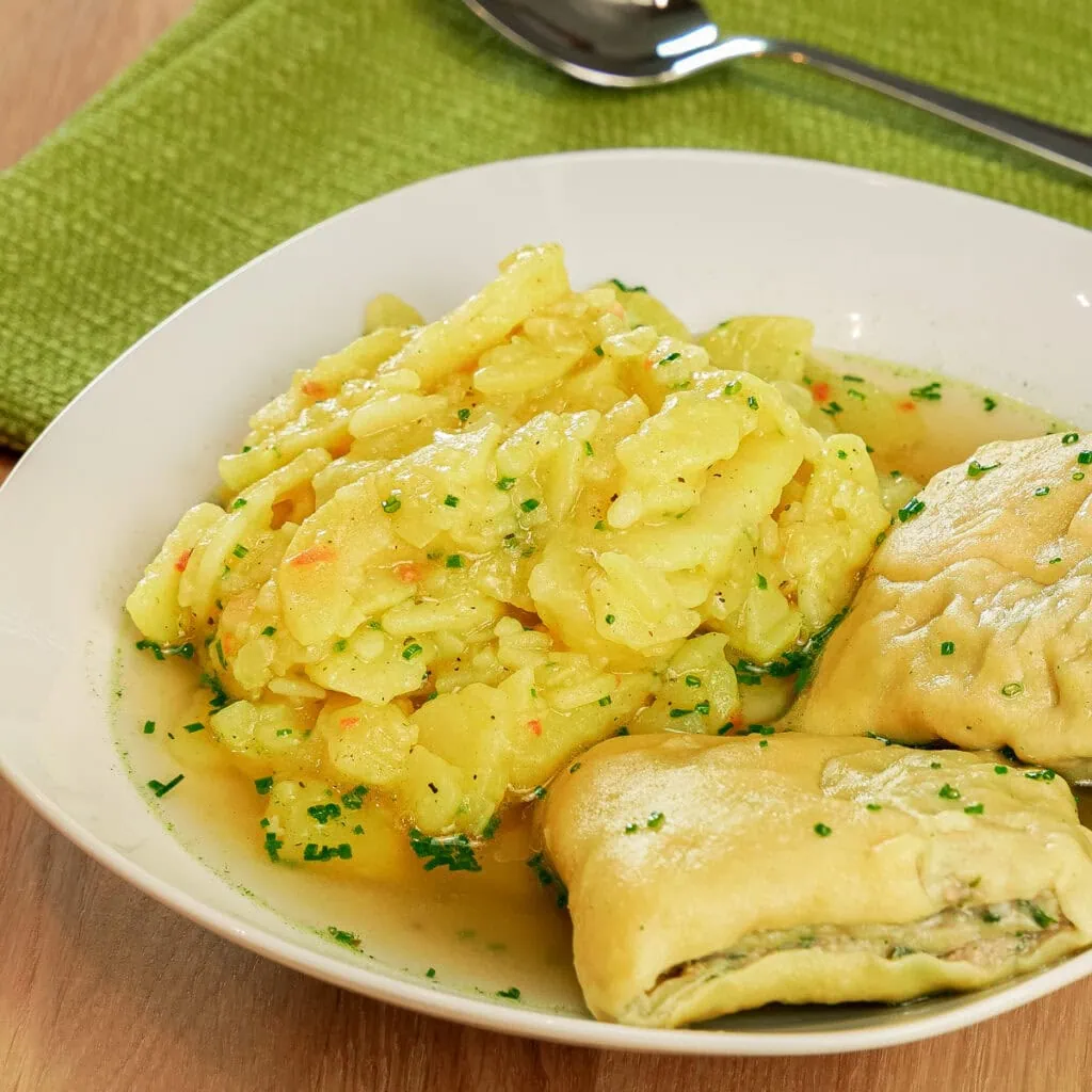 Schwäbischer Kartoffelsalat mit Brühe, serviert mit Maultaschen auf einem Teller.