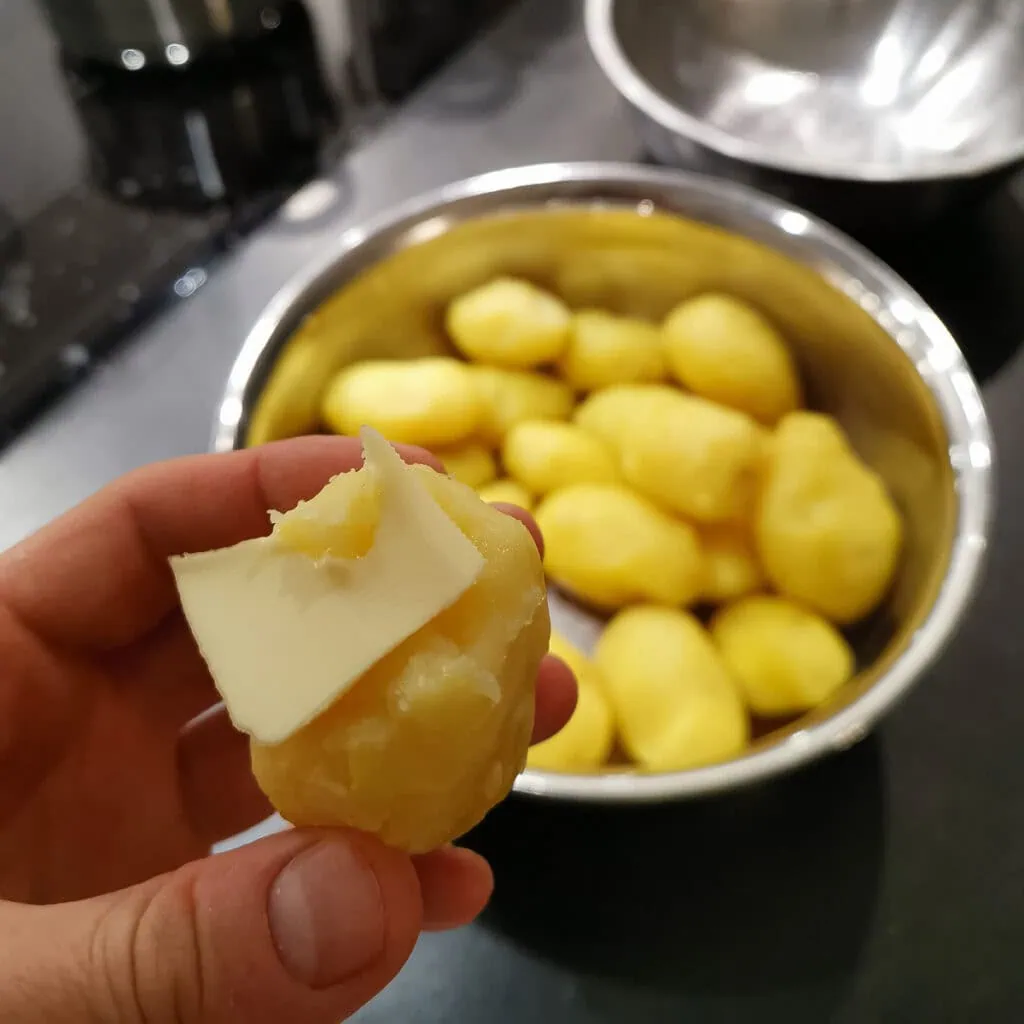 Geschälte Kartoffel in der Hand mit einem Stück Butter darauf.