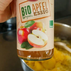 Eine Flasche Bio Apfelessig wird über die Kartoffelscheiben gegossen.