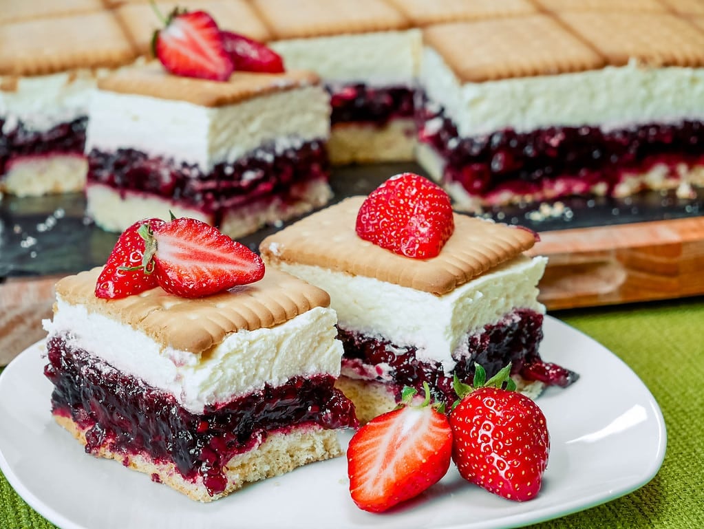 Schichten von Butterkekskuchen mit Roter Grütze, dekoriert mit frischen Erdbeeren, auf einem Teller.