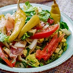 Ein Teller mit griechischem Bauernsalat, bestehend aus frischen Tomaten, Gurken, Zwiebeln, Paprika, Blattsalat und Peperoni.