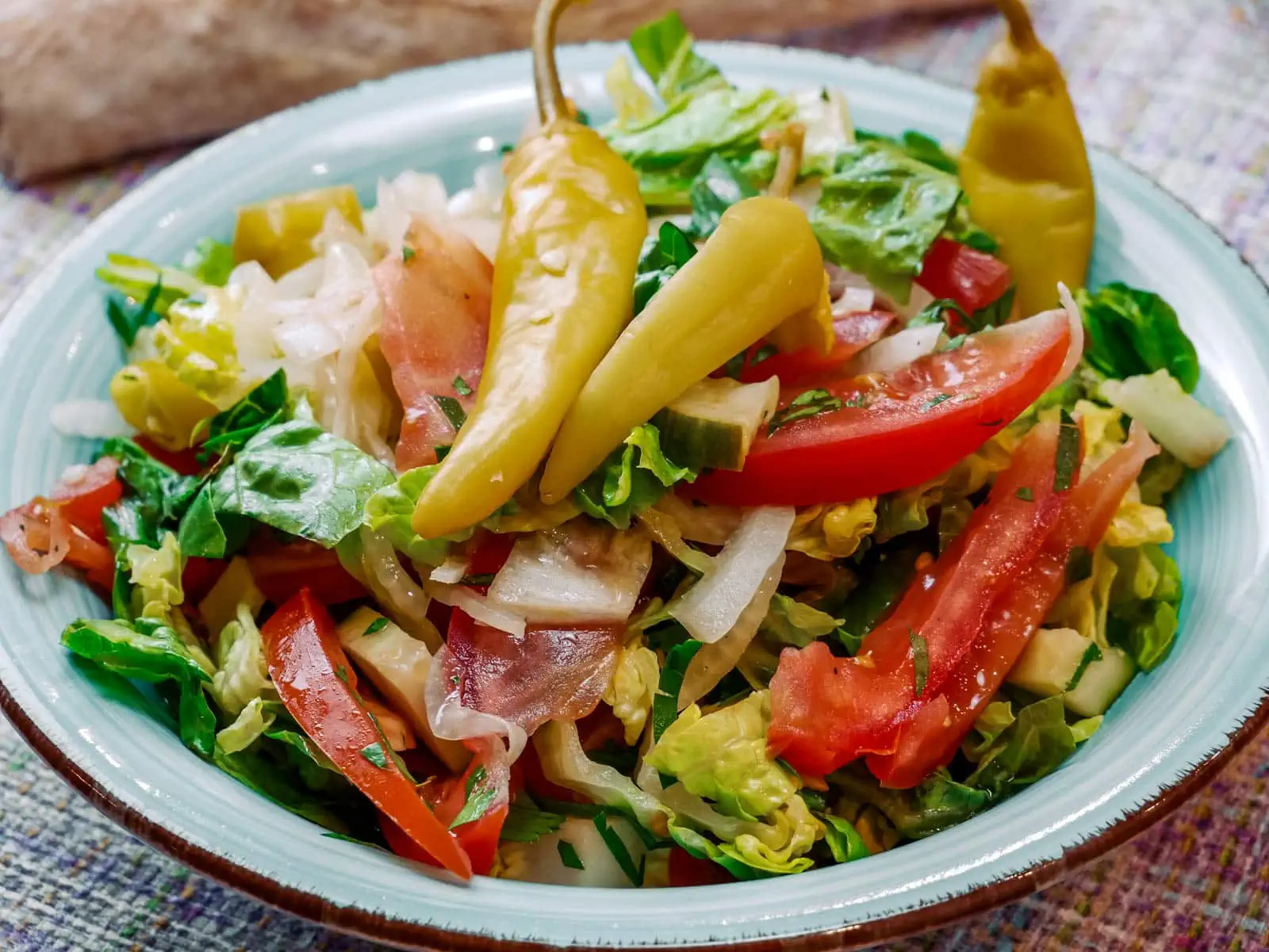 Ein Teller mit griechischem Bauernsalat, bestehend aus frischen Tomaten, Gurken, Zwiebeln, Paprika, Blattsalat und Peperoni.