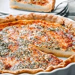 Eine Quiche aus einer Rahm-Schnittlauch-Käse-Masse, gebacken in einem knusprigen Teig, serviert in einer Tarteform.