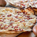 Ein knuspriger Elsässer Flammkuchen, belegt mit Speck und Zwiebeln, auf einem Backblech.