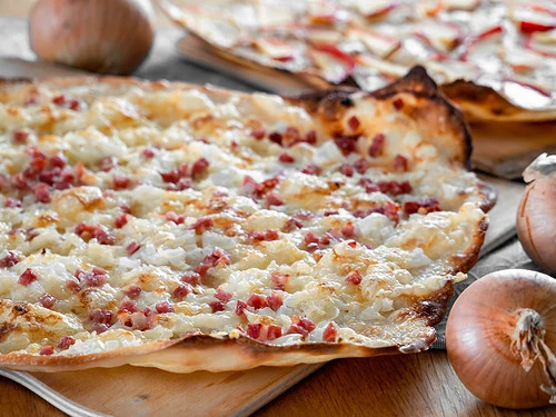 Ein knuspriger Elsässer Flammkuchen, belegt mit Speck und Zwiebeln, auf einem Backblech.