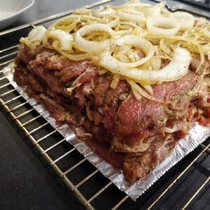 Der Gyros-Schichtbraten im Ofen, mit Zwiebelscheiben belegt, bereit zum Backen.