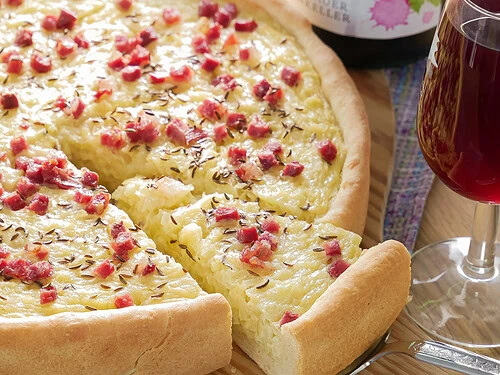 Ein angeschnittener schwäbischer Zwiebelkuchen mit Speck und Kümmel, serviert auf einem Holzbrett.