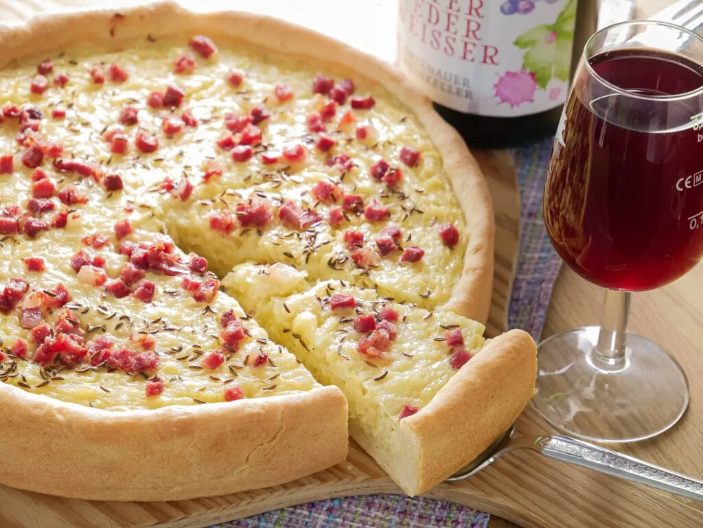 Schwäbischer Zwiebelkuchen, serviert mit einem Glas Federweißer und einer Flasche Federweißer im Hintergrund.