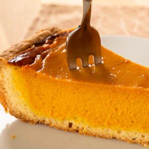 Ein Stück Pumpkin Pie, auf das eine Gabel in die cremige Füllung gedrückt wird.