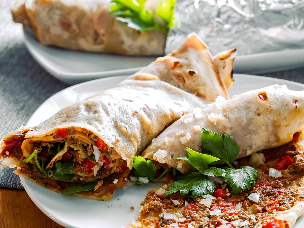 Eine gefüllte Lahmacun-Rolle mit Hackfleisch, Gemüse und Kräutern, auf einem Teller serviert.