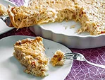 Ein Stück Sauerkraut-Quiche auf einem Teller, mit knusprigem Teig und einer herzhaften Füllung aus Sauerkraut und Speck. Im Hintergrund steht die restliche Quiche in einer weißen Tarteform.