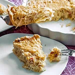 Ein Stück Sauerkraut-Quiche auf einem Teller, mit knusprigem Teig und einer herzhaften Füllung aus Sauerkraut und Speck. Im Hintergrund steht die restliche Quiche in einer weißen Tarteform.