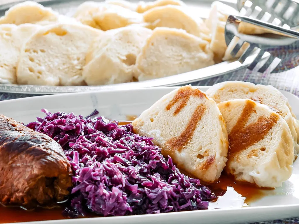 Schwäbische Hefeknöpfle, serviert mit Rotkohl und Bratensauce, auf einem Teller mit Besteck im Hintergrund.