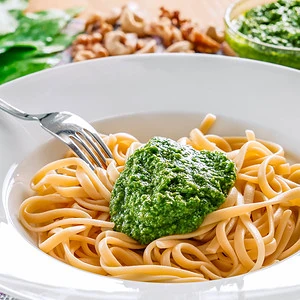 Ein Teller mit Spaghetti und einem Klecks grünem Bärlauch Pesto, garniert mit einer Gabel, die teilweise unter der Pasta verborgen ist, auf einem Tisch mit unscharfem Hintergrund.