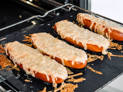 Drei frisch gebackene Käse-Laugenstangen auf einem Backblech im Ofen, überzogen mit geschmolzenem Käse.