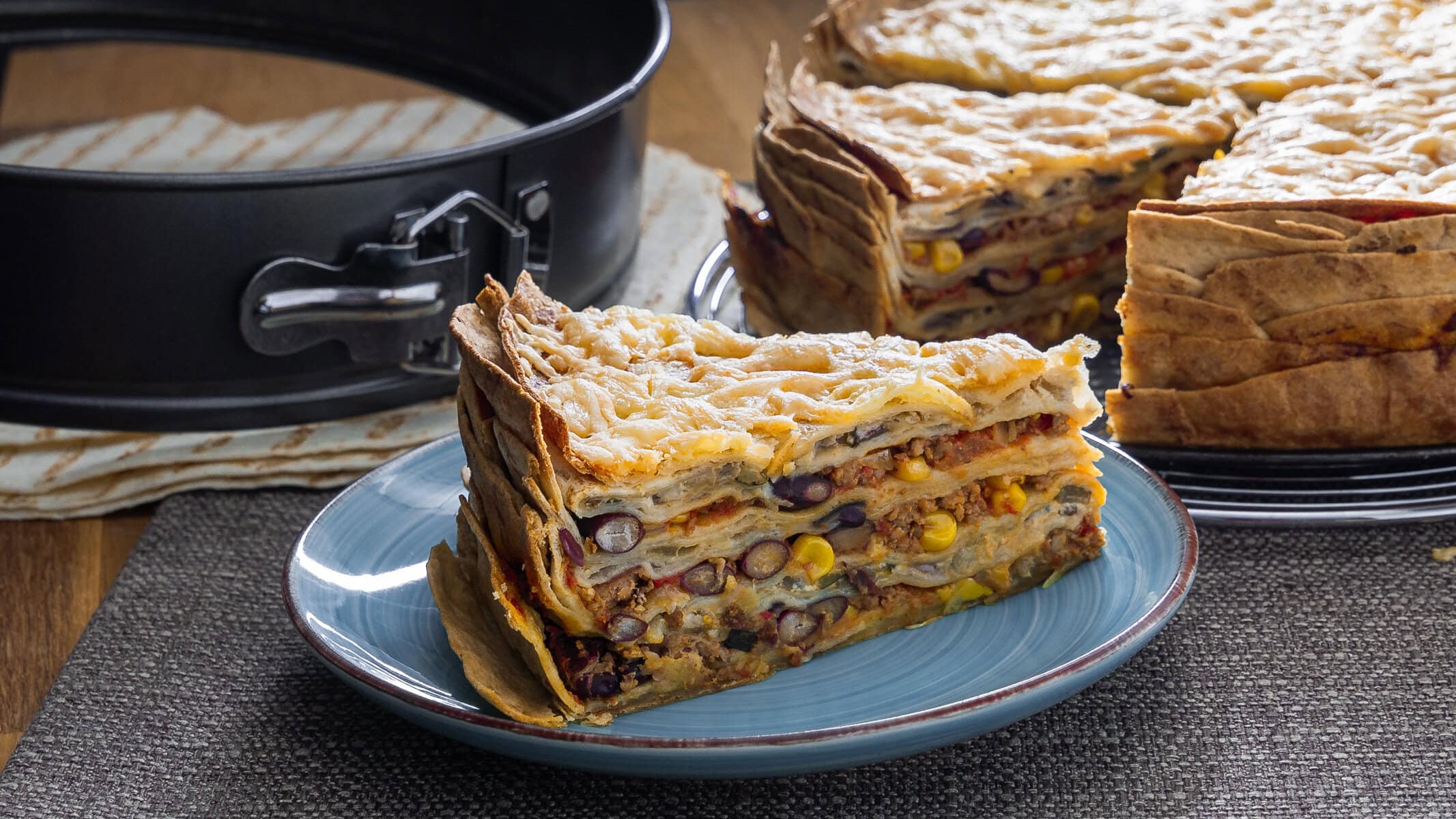 Herzhafte Mexikanische Tortilla Lasagne mit einer goldenen Käseschicht, serviert auf einem blauen Teller.